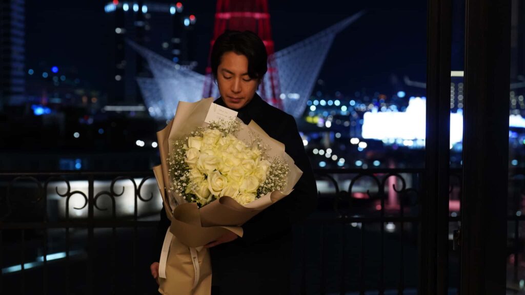 神戸の夜景を背景に白い薔薇の花束を持つ代表フローリスト日坂亮太