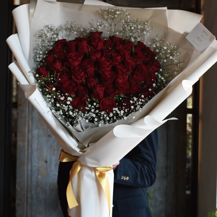 白いラッピングとゴールドのリボンで包んだ50本の赤い薔薇の花束