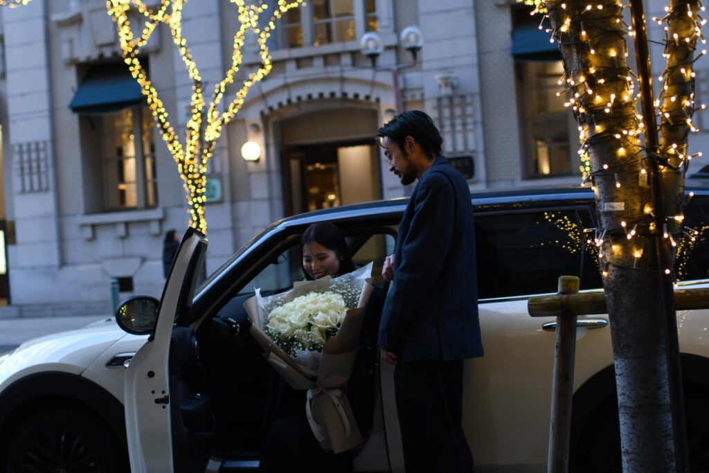 車のそばで大きな白い薔薇の花束を持つカップル